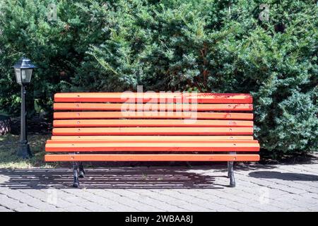 Orange wooden bench with forged metal legs in the park on a green wooden background Stock Photo