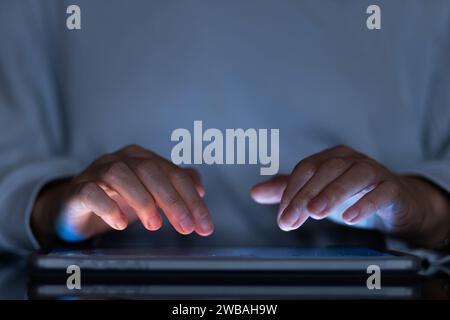 female hands typing on a tablet in a dark office room, close-up Stock Photo