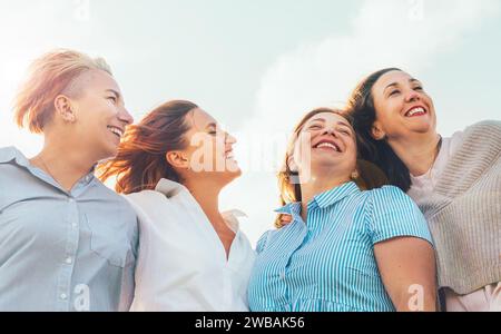 Portrait of four cheerful smiling and laughing women embracing during sunset time outdoors walking by the green hill. Woman's friendship, relations, a Stock Photo