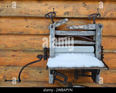 An antique chair is situated against a white wall outdoors, blanketed in a layer of freshly fallen snow Stock Photo