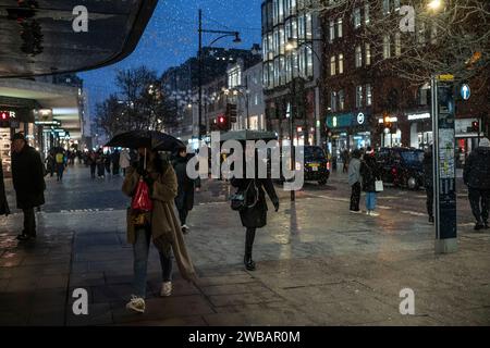 Shoppers brave the cold winter weather during freezing sleet and rain showers on Oxford Street, London's busiest high Street, England, United Kingdom Stock Photo