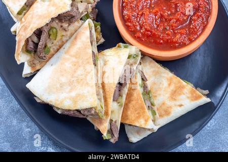 Mexican cuisine fajita quesadilla with pieces of beef steak, green bell pepper, onion and cheese, served with salsa sauce and sour cream, top view, horizontal Stock Photo