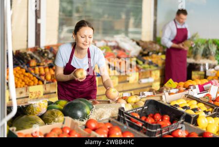 Smiling saleswoman laying out apples on counter in supermarket Stock Photo