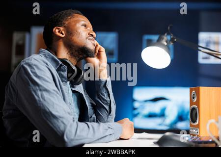 At home, independent contractor exhausted and yawning, attempting to focus under stress to fulfill a due date. African american researching internet statistics to deal with operations. Stock Photo