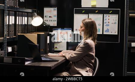 Arriving at workplace, caucasian woman with experience in criminal investigation. Young female private investigator with laptop bag enters office and takes a seat, ready to conduct crime case study. Stock Photo