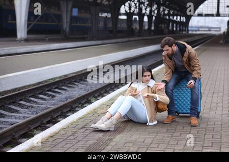Being late. Worried couple with suitcase waiting at train station, space for text Stock Photo