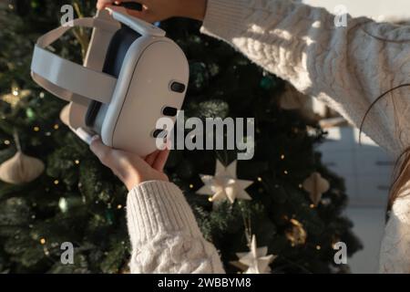 In front of a Christmas tree, a girl is holding a virtual reality headset. Stock Photo