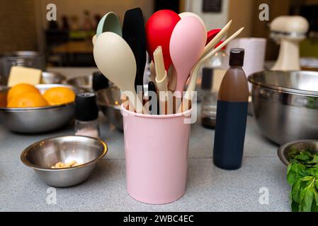 A variety of kitchen utensils including spatulas and brushes in a pink holder, neatly organized on a countertop among cooking ingredients. Stock Photo