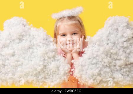 Cute little girl dressed as cupid with clouds on yellow background. Valentine's Day celebration Stock Photo