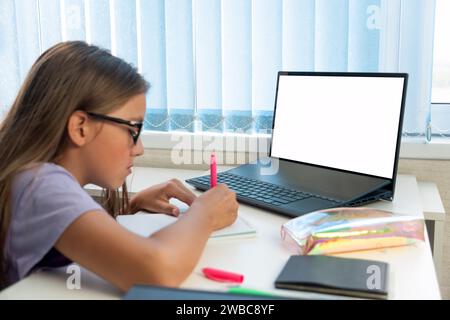 Primary school Student child writing in book using laptop. Distance learning online education. girl studying at home with digital tablet computer and Stock Photo