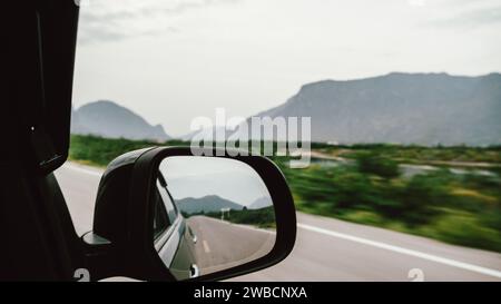 A close-up of a car rear view mirror while driving on an asphalt road or a freeway. Stock Photo