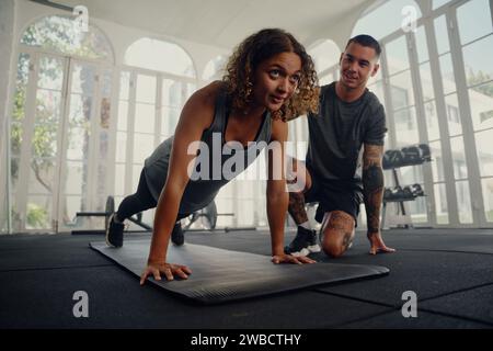Multiracial trainer with young woman in sports clothing doing push-up exercises at the gym Stock Photo