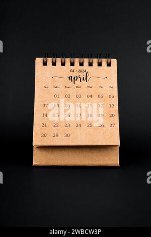 2024 April brown desk calendar on black background. Stock Photo