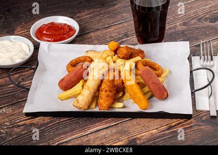 Snack plate with french fries, crispy chicken, cheese sticks, sausage and spring rolls on wooden table Stock Photo