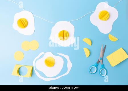 three fried eggs paper craft hanging from a string on a blue background, easter decoration concept,  Stock Photo