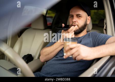 Bearded man using smartphone and talking on the speaker while driving car. Male driver talking on in-car speakerphone Stock Photo