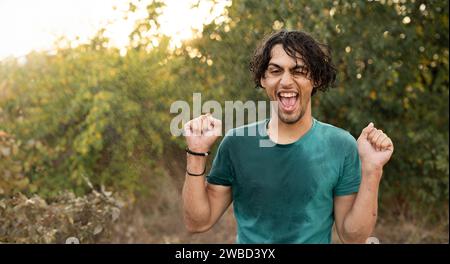 Smiling young man during the rain in the park. Guy enjoying the rain outdoors, has a joyful expression during the rainy weather. Stock Photo