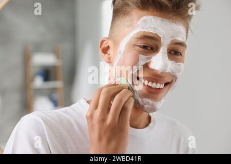 Happy young man washing off face mask with sponge on white background ...