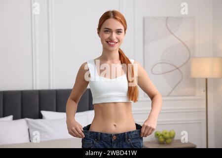 Slim woman wearing big jeans in room. Weight loss Stock Photo