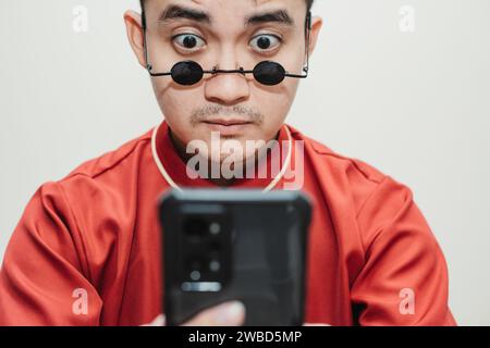 Asian man wearing Cheongsam and black rounded vintage sunglasses is looking at his smartphone Stock Photo