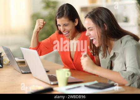 Two excited tele workers celebrating success online checking laptop at home Stock Photo