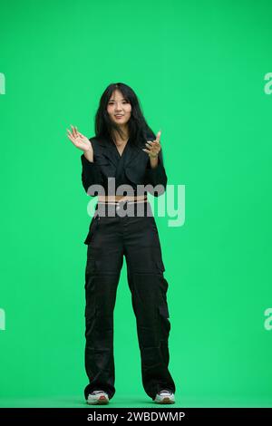A woman in black clothes, on a green background, in full height, claps Stock Photo