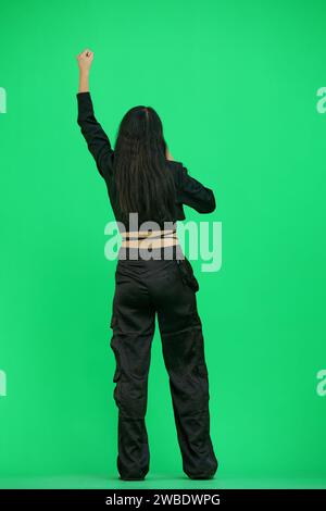 A woman in black clothes, on a green background, in full height, screams Stock Photo