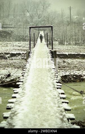 Spulber, Vrancea County, Romania, approx. 1996. Man crossing a wooden bridge over Zabala River in a winter day. Stock Photo