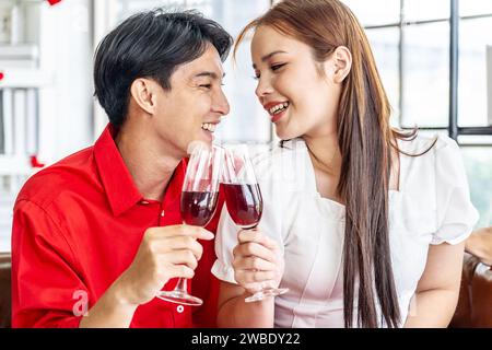 Cheerful happy beautiful loving asian couple relaxing together, smiling man and woman sitting on couch, drinking red wine, celebration Stock Photo