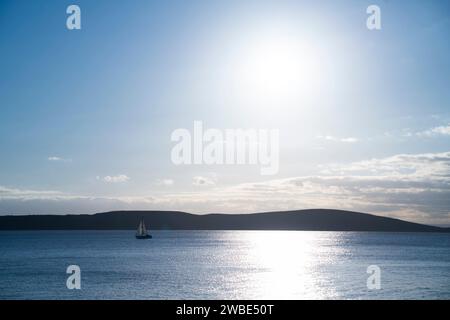A sailing boat sails across the bay of Weston-super-Mare, North Somerset with Brean Down in the background at sunset. Stock Photo
