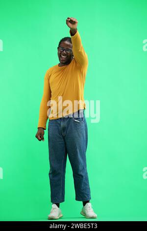 A man in a yellow jacket on green background raised his hand up Stock Photo
