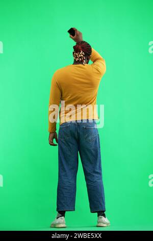 A man in a yellow jacket on a green background waves a phone, back view Stock Photo