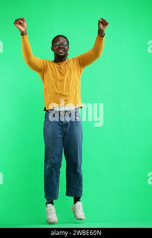 A man in a yellow jacket jumps on a green background Stock Photo