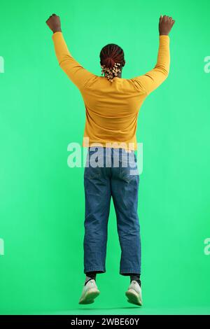 A man in a yellow jacket jumps on a green background, back view Stock Photo