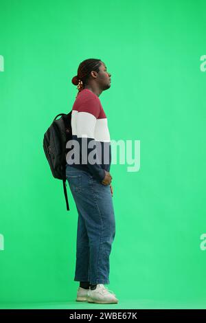 A man in a multi-colored jacket with a backpack on a green background, in profile Stock Photo