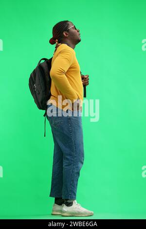 man in a yellow sweater with a backpack on a green background, in profile Stock Photo