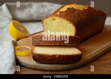 Delicious homemade sliced pound lemon cake with half of lemon on a cutting board on a wooden background. Stock Photo