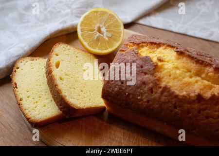 Delicious homemade sliced pound lemon cake with half of lemon on a cutting board on a wooden background. Stock Photo