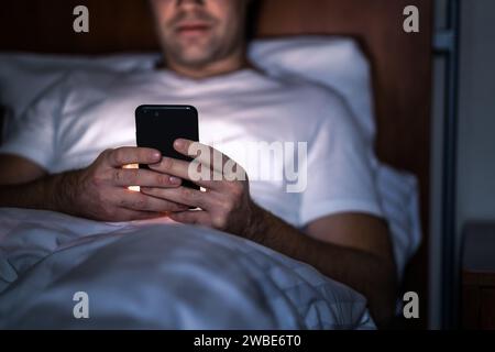 Phone in bed at night. Man with smartphone before sleeping. Secret texting, cheating or working late. Happy guy browsing online news. Stock Photo