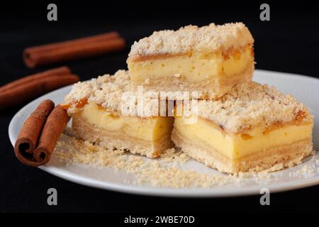 Sliced apple pie made from shortcrust pastry with cottage cheese cream and apple wedges on a white plate on a black background. cinnamon sticks Stock Photo