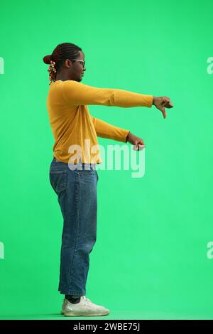 A man in a yellow sweater on a green background shows thumbs down in profile Stock Photo