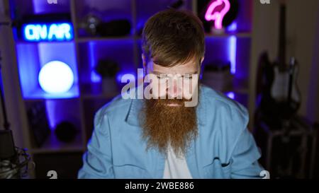 Handsome, serious-faced redhead guy sitting in a dimly lit gaming room late into the night, fully absorbed in the cyber world of advanced video games Stock Photo