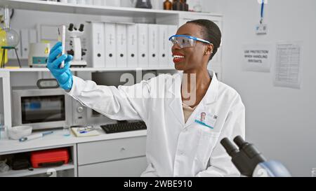 Beautiful african american woman scientist engaged in a video call conversation in the lab, deep into research analysis, sitting with smartphone, and Stock Photo