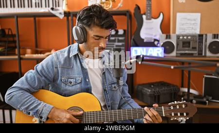 Handsome hispanic man playing guitar in a music studio with microphone and headphones Stock Photo