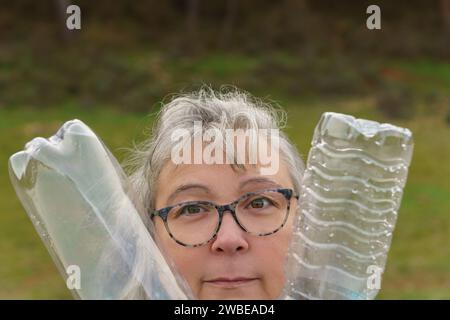 close-up of an older white-haired woman with glasses holding two empty plastic bottles collected in the field, concept of ecology Stock Photo