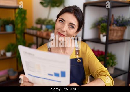 Middle age hispanic woman florist reading document at flower shop Stock Photo