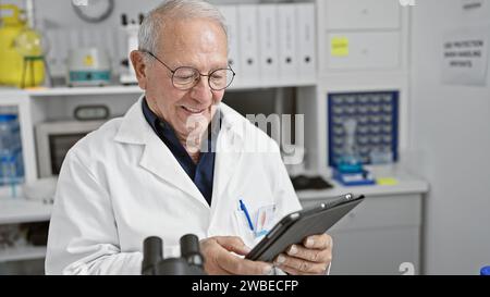 Senior man scientist smiling confident using touchpad at laboratory Stock Photo