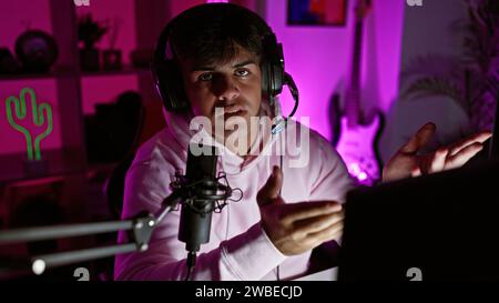 Attractive young hispanic man streaming into the night, deep in conversation, gaming headset on, engrossed in digital entertainment, seated in his dar Stock Photo