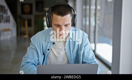 A focused young hispanic man in headphones works on his laptop at a modern university library. Stock Photo