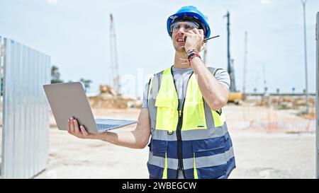 Young hispanic man architect talking on walkie-talkie using laptop at construction place Stock Photo